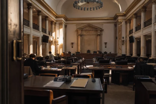 Salle de conseil municipal charentaise-maritime avec tables de réunion, dossiers et micros sous une lumière d’hiver rasante.