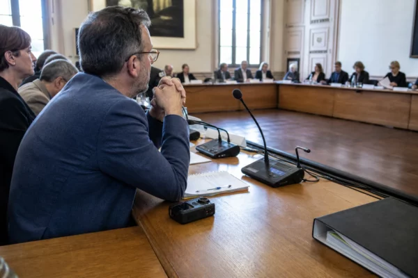 Salle municipale française avec chaise vide, micros et dossiers flous, évoquant une enquête sur la police municipale