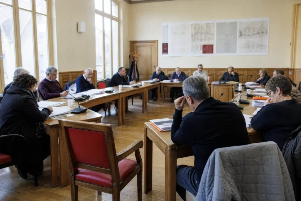 Salle de conseil municipal française avec élus anonymes, micros, dossiers et une chaise vide en vue oblique