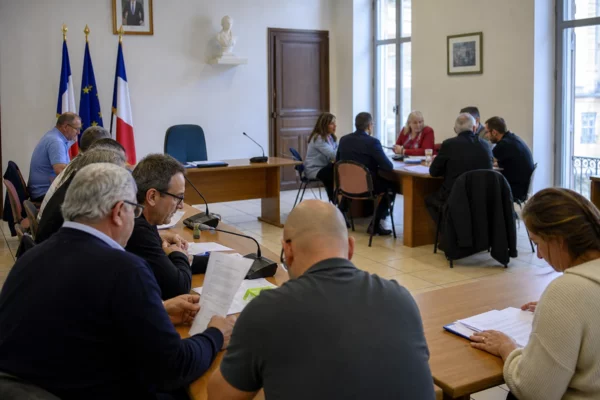 Salle de conseil municipal française avec une chaise vide, des micros et des dossiers lors d’une réunion politique