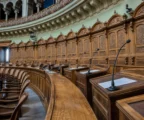 Salle de débat française vide, pupitres alignés, micros et feuilles blanches, dans un grand décor institutionnel.