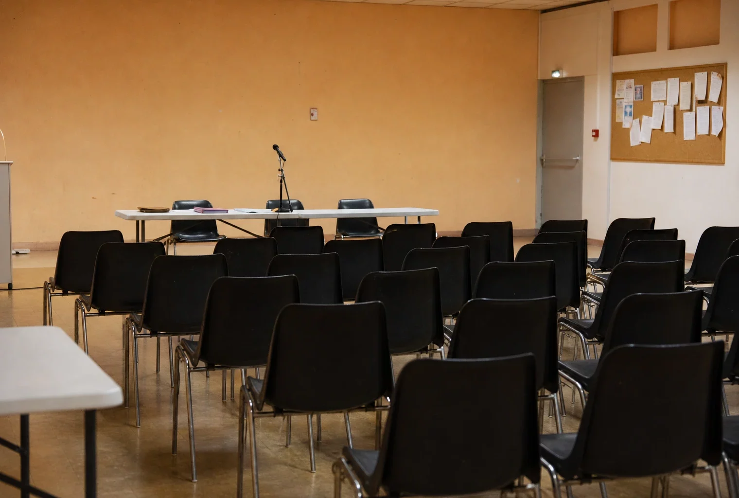 Salle municipale vide avec des chaises alignées et une table de prise de parole, avant une réunion politique à Carpentras