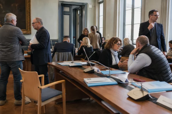 Salle municipale française avec élus anonymes, micros et chaise vide lors d’une réunion politique locale