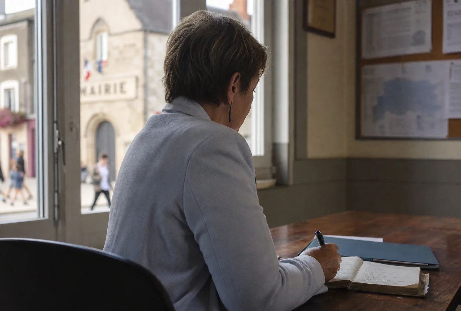 Élue locale anonyme prenant des notes dans une mairie française, avec une rue en arrière-plan