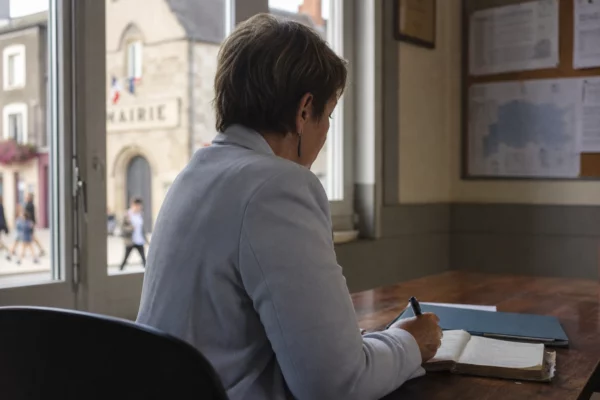 Élue locale anonyme prenant des notes dans une mairie française, avec une rue en arrière-plan