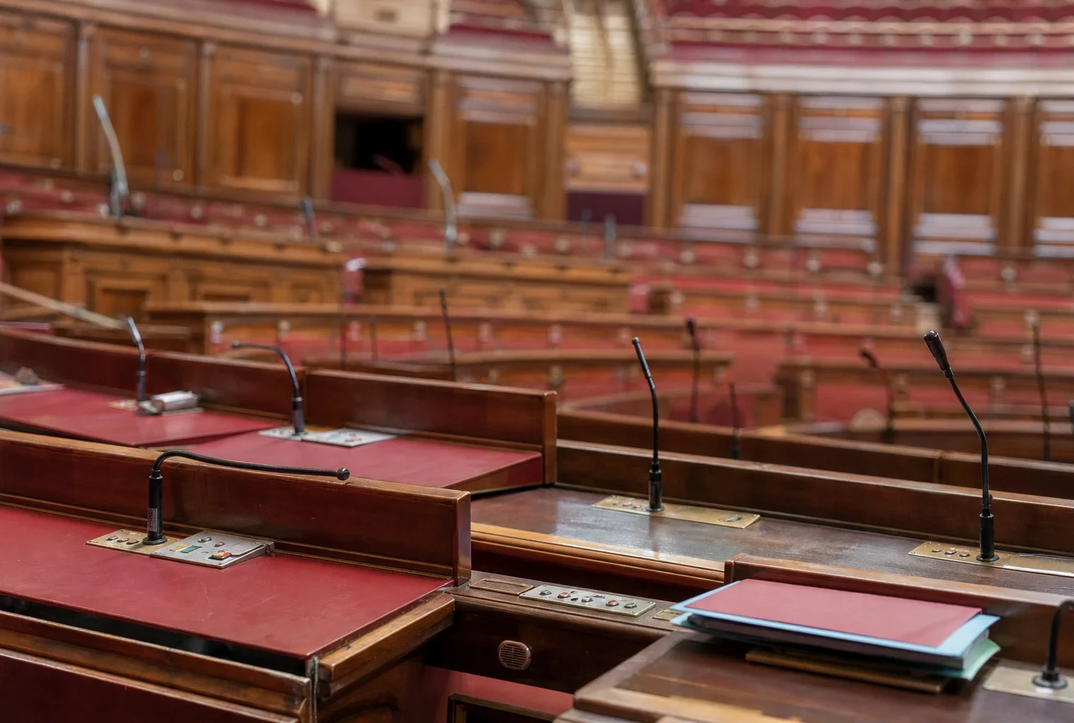 Salle des séances du Sénat vide au Palais du Luxembourg, avec pupitres rouges et micros alignés.