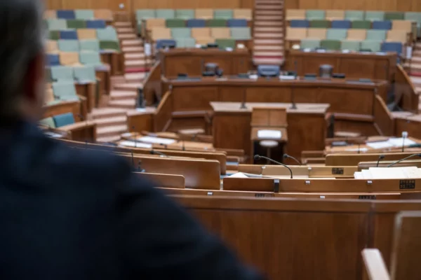 Hémicycle du Sénat vide, rangées de sièges en bois et pupitre central sous une lumière douce et uniforme.