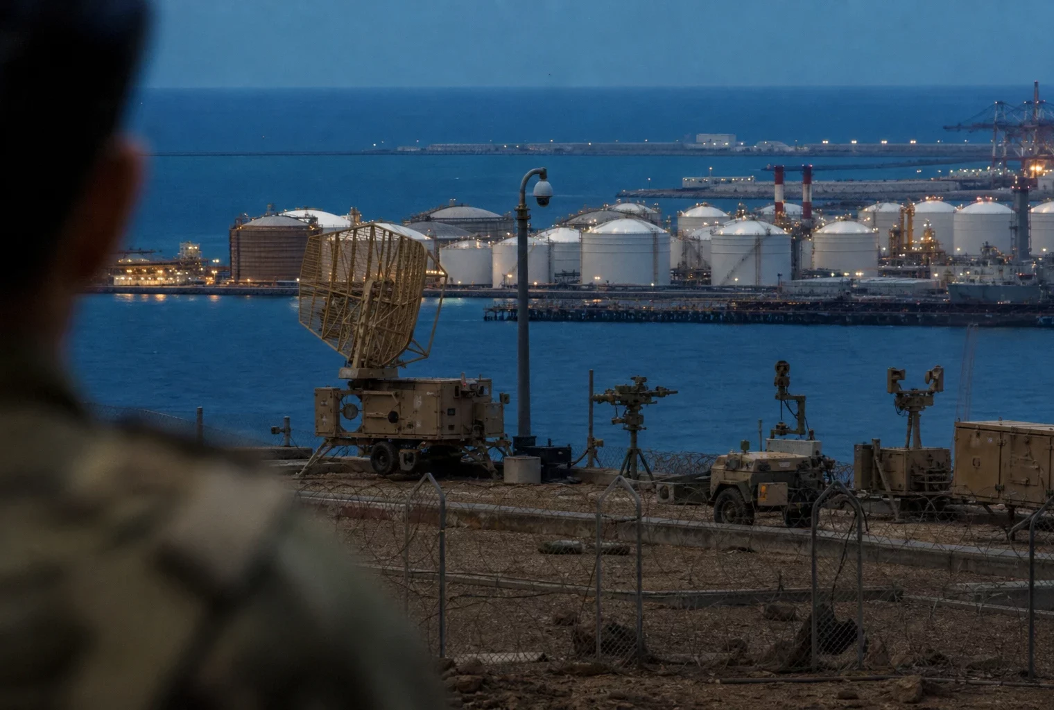 Radar et équipements militaires au premier plan d’un site énergétique à Yanbu, avec réservoirs et tuyauteries en arrière-plan.