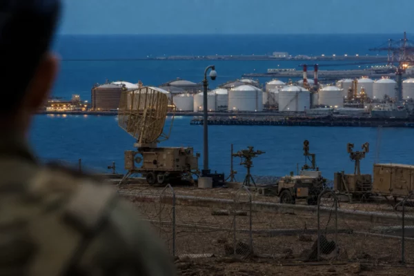 Radar et équipements militaires au premier plan d’un site énergétique à Yanbu, avec réservoirs et tuyauteries en arrière-plan.