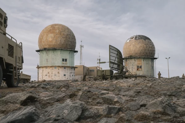 Base militaire à Yanbu avec radars à dôme, engins au sol et bâtiments techniques sous un ciel laiteux.
