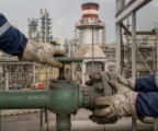 Mains gantées réglant une vanne sur un oléoduc de Yanbu, au milieu de tuyauteries et structures industrielles usées.