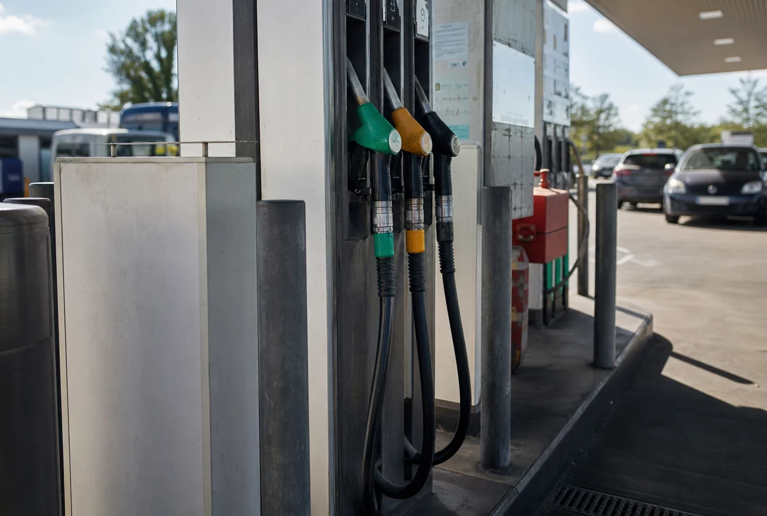 Une pompe de station-service avec son pistolet de carburant, devant des voitures en attente.