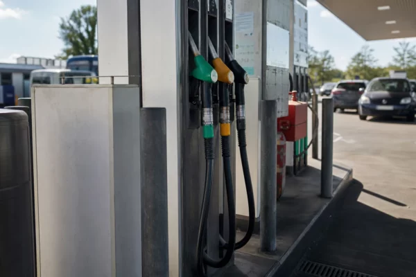 Une pompe de station-service avec son pistolet de carburant, devant des voitures en attente.