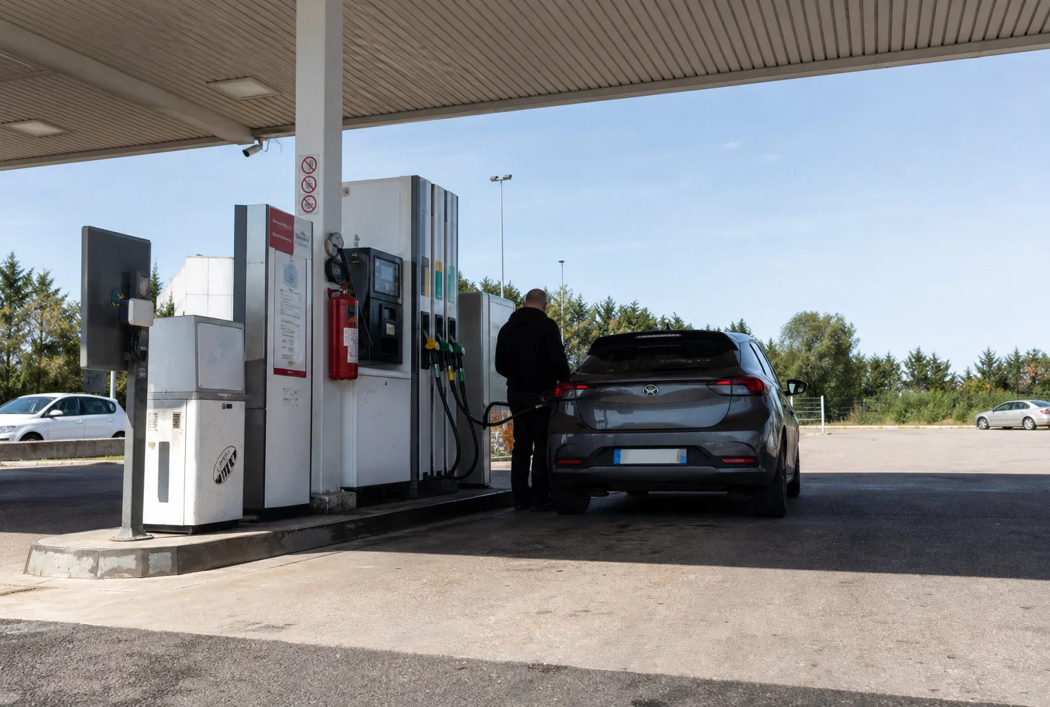 Pompes d’une station-service en bord de route, avec un automobiliste qui attend près de sa voiture.