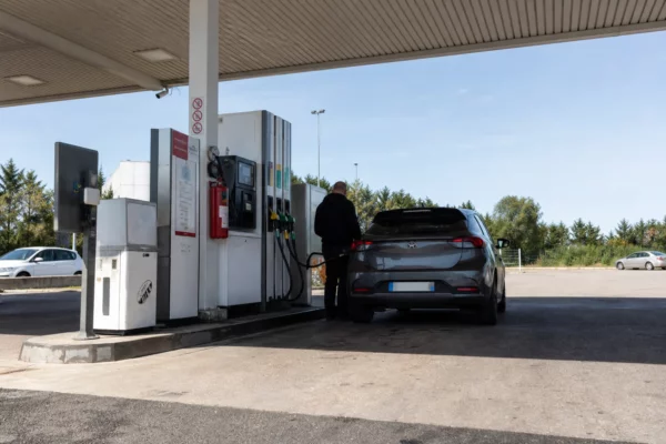 Pompes d’une station-service en bord de route, avec un automobiliste qui attend près de sa voiture.