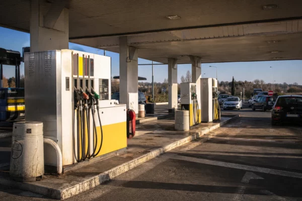 Pompes d’une station-service avec panneaux de prix, dans un contexte banal de route, pour illustrer le coût du carburant.