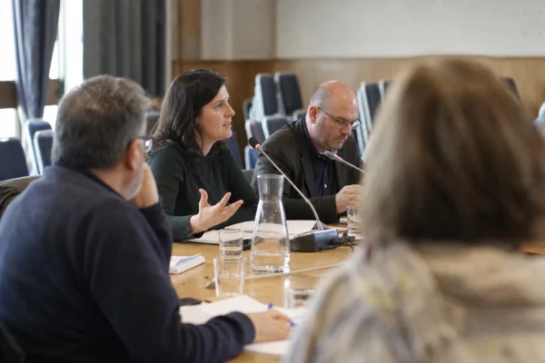 Une table ronde politique dans une salle de réunion, avec micros et participants assis autour d’une table ovale.
