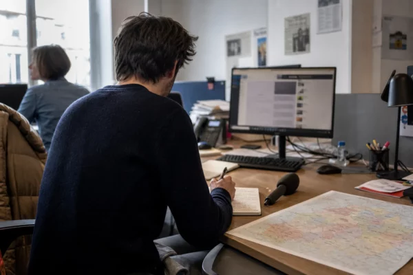 Journaliste préparant un sujet politique dans une rédaction locale française, avec carnet, carte floue et micro sans logo