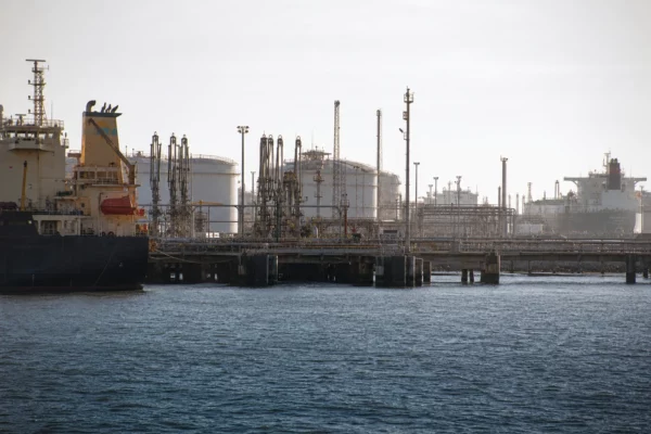 Terminal pétrolier saoudien en activité, cuves, tuyauteries et bras de chargement devant des tankers et quais industriels.