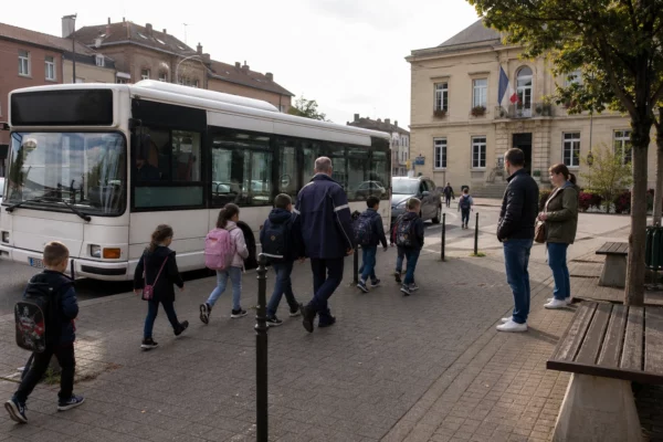 Enfants avec leurs cartables près d’un bus scolaire dans une rue de Hayange, accompagnés par un adulte