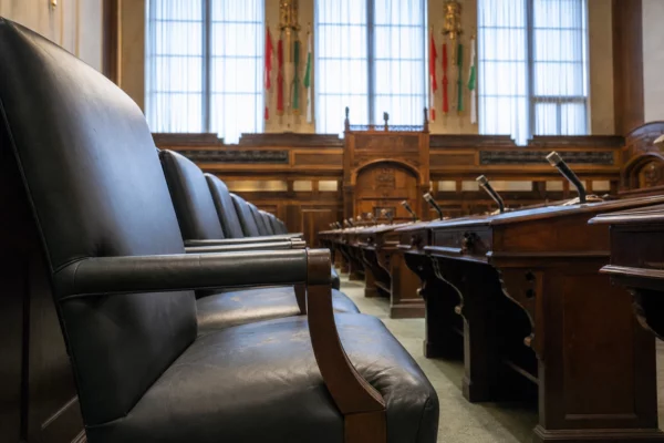 Salle d’audience vide du tribunal correctionnel, bancs en cuir, tables de défense et tribune sous lumière froide.