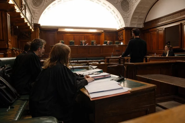 Salle d’audience du tribunal correctionnel de Paris, tables d’avocats, dossiers ouverts, micros et bancs sous lumière rasante.