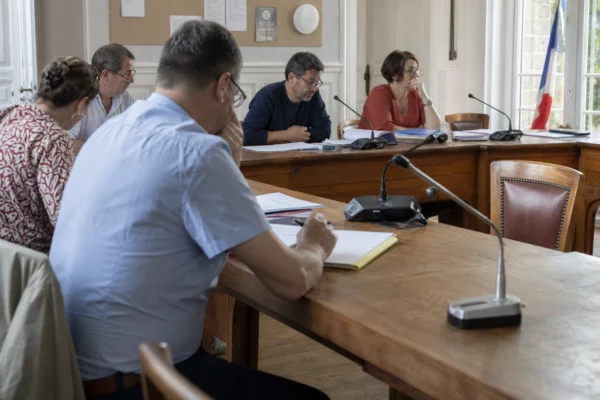 Conseil municipal français avec une chaise vide, des micros et des dossiers évoquant les négociations de la gauche