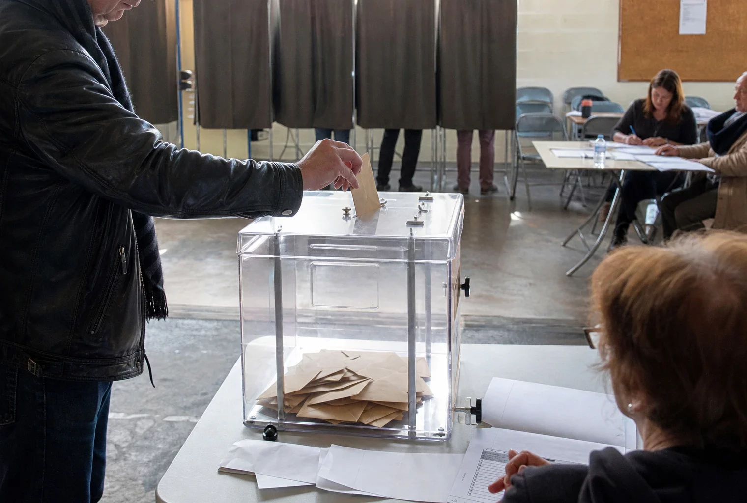 Une urne de vote dans une salle municipale, avec isoloirs et table de dépouillement pour des grands électeurs.