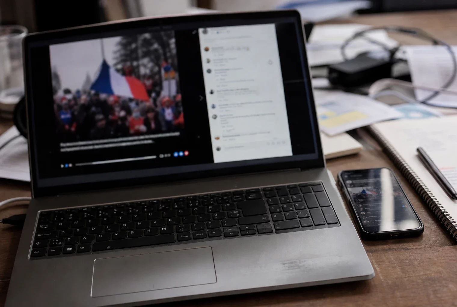 Un téléphone et un ordinateur affichent une vidéo politique partagée, sur une table de campagne avec des papiers épars.