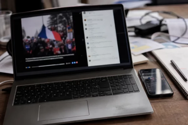 Un téléphone et un ordinateur affichent une vidéo politique partagée, sur une table de campagne avec des papiers épars.