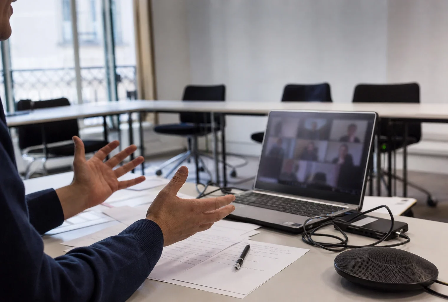 Salle de réunion avec ordinateur ouvert en visioconférence, feuilles et câbles sur la table, pour un vote interne de parti.