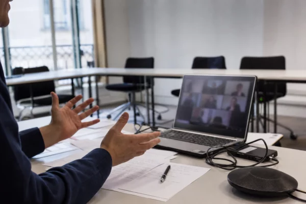 Salle de réunion avec ordinateur ouvert en visioconférence, feuilles et câbles sur la table, pour un vote interne de parti.