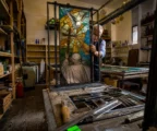 Dans un atelier de verrier en France, un grand vitrail contemporain se monte parmi outils, châssis et tables encombrées.