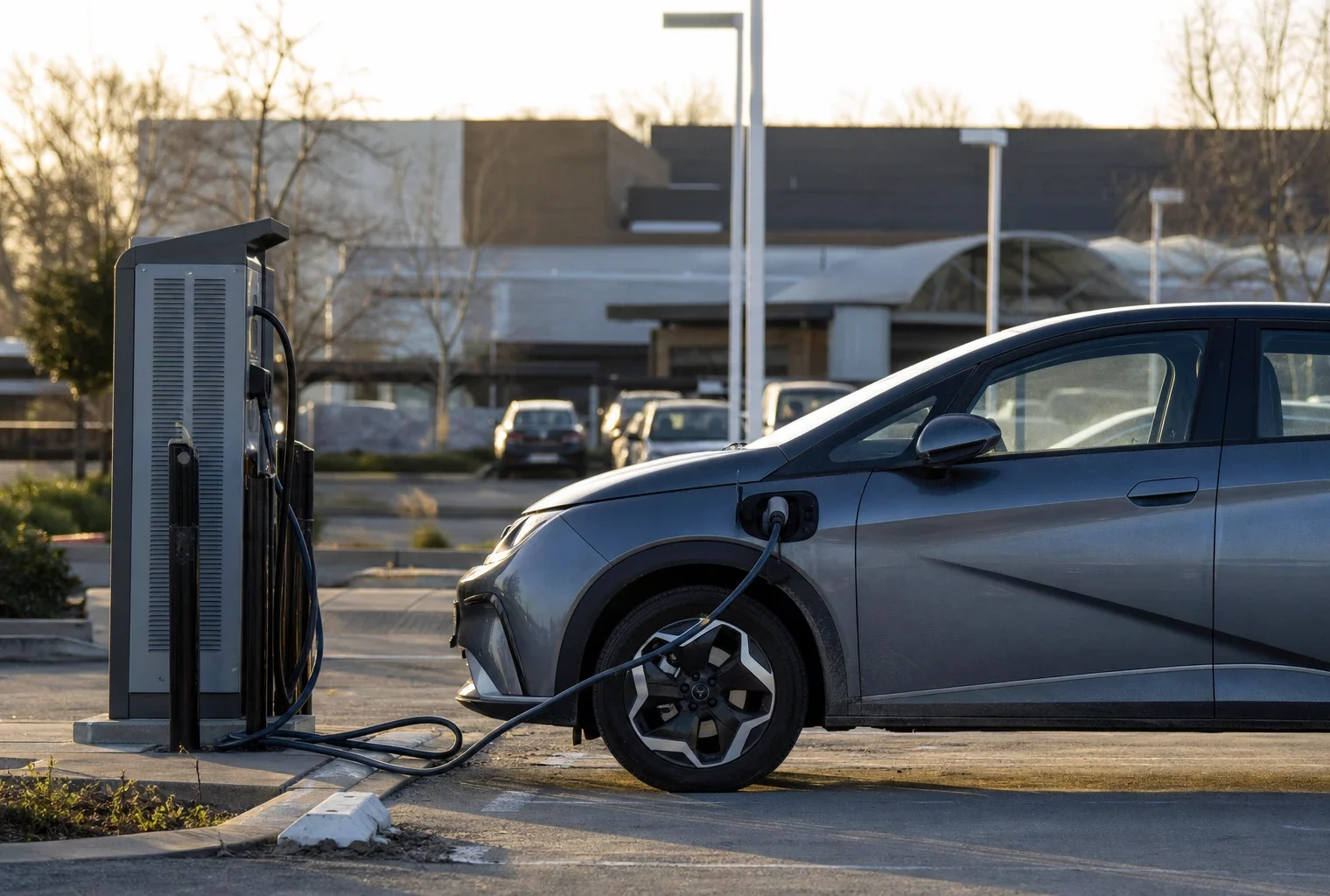 Une voiture électrique branchée sur une borne de recharge, dans un parking de zone périurbaine.