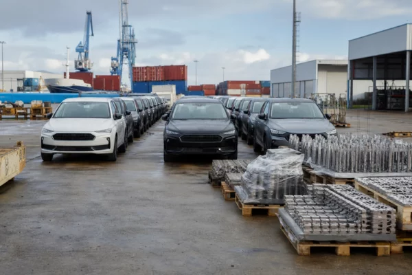 Voitures et pièces automobiles stockées dans un port de commerce, avec conteneurs et installations logistiques.