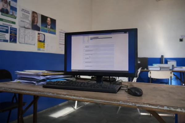 Un ordinateur ouvert affiche un formulaire de vote dans une permanence politique, avec des papiers de campagne autour.