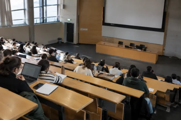 Amphithéâtre universitaire avec rangées de sièges fixes, pupitre de cours et équipement audiovisuel dans une salle d’enseignement.
