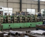 Des pièces métalliques d’équipement militaire en assemblage sur une ligne de production usée, dans un atelier industriel lumineux.