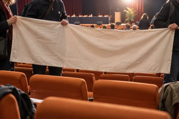 Des mains de militants tiennent une banderole vierge devant des rangées de fauteuils et une estrade de congrès politique.