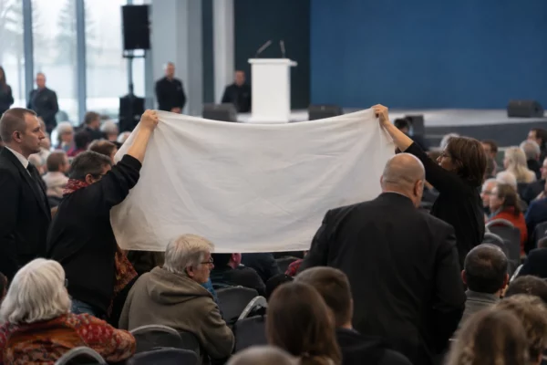 Une banderole unie est tenue entre les rangées de chaises d’une salle de meeting, près d’agents de sécurité.