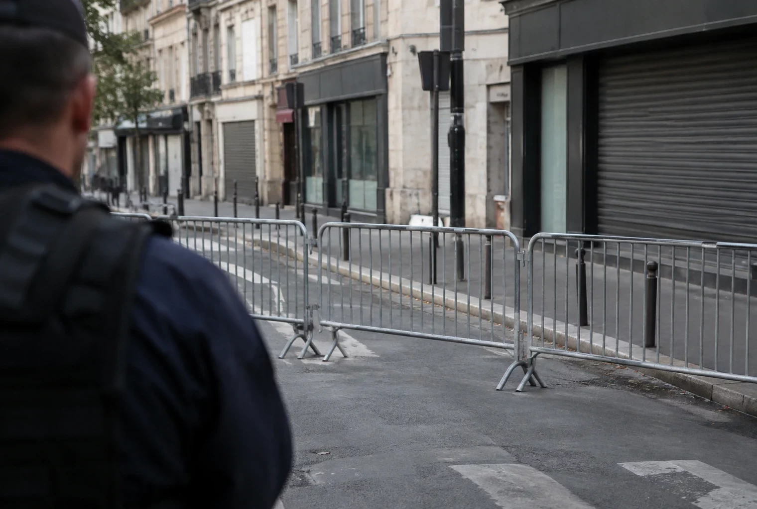 Barrières mobiles alignées sur une rue urbaine, devant des façades et des commerces sans enseigne lisible.