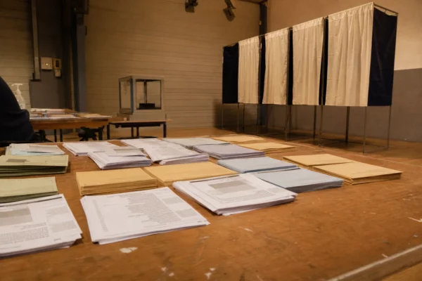 Des bulletins de vote sont disposés sur les tables d’un bureau de vote, avec les isoloirs au fond.