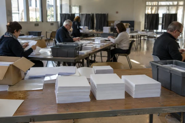 Piles de bulletins vierges sur une table de préparation, près de bacs de tri et de matériel de mise sous pli.