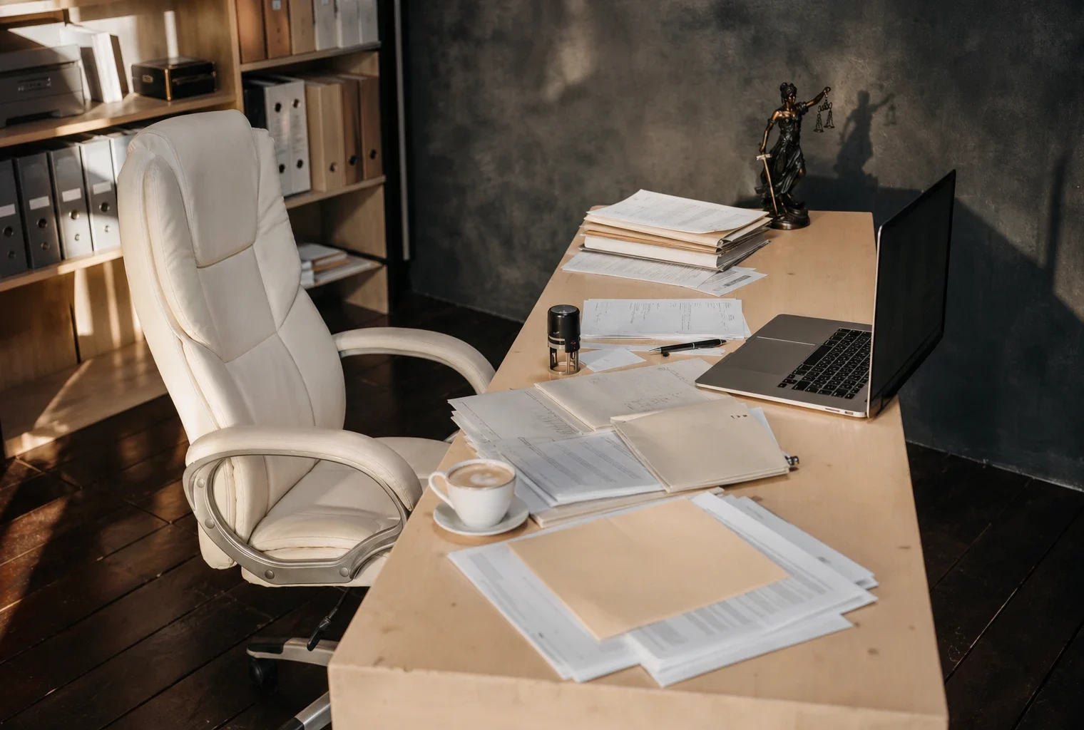 Bureau de commissaire de justice vu de haut, avec ordinateur ouvert, dossiers imprimés, tampon et étagère de classeurs.