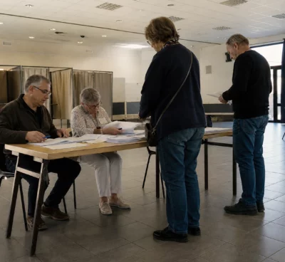 Bureau de vote installé dans une salle municipale pour une primaire, avec table d’émargement et isoloirs.