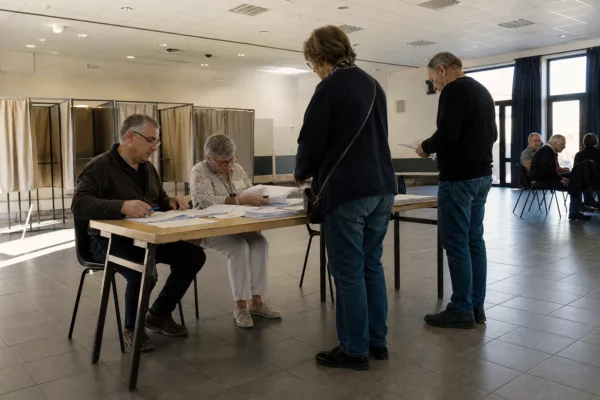 Bureau de vote installé dans une salle municipale pour une primaire, avec table d’émargement et isoloirs.