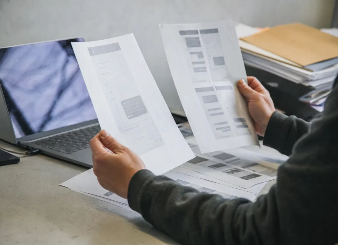 Des captures d’écran contestées et des documents imprimés posés sur une table de travail, avec un ordinateur ouvert à côté.