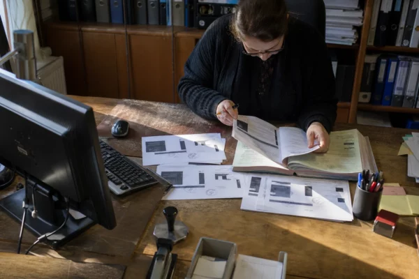 Des captures d’écran imprimées sont posées sur un dossier dans un cabinet, au milieu de pièces de vérification.