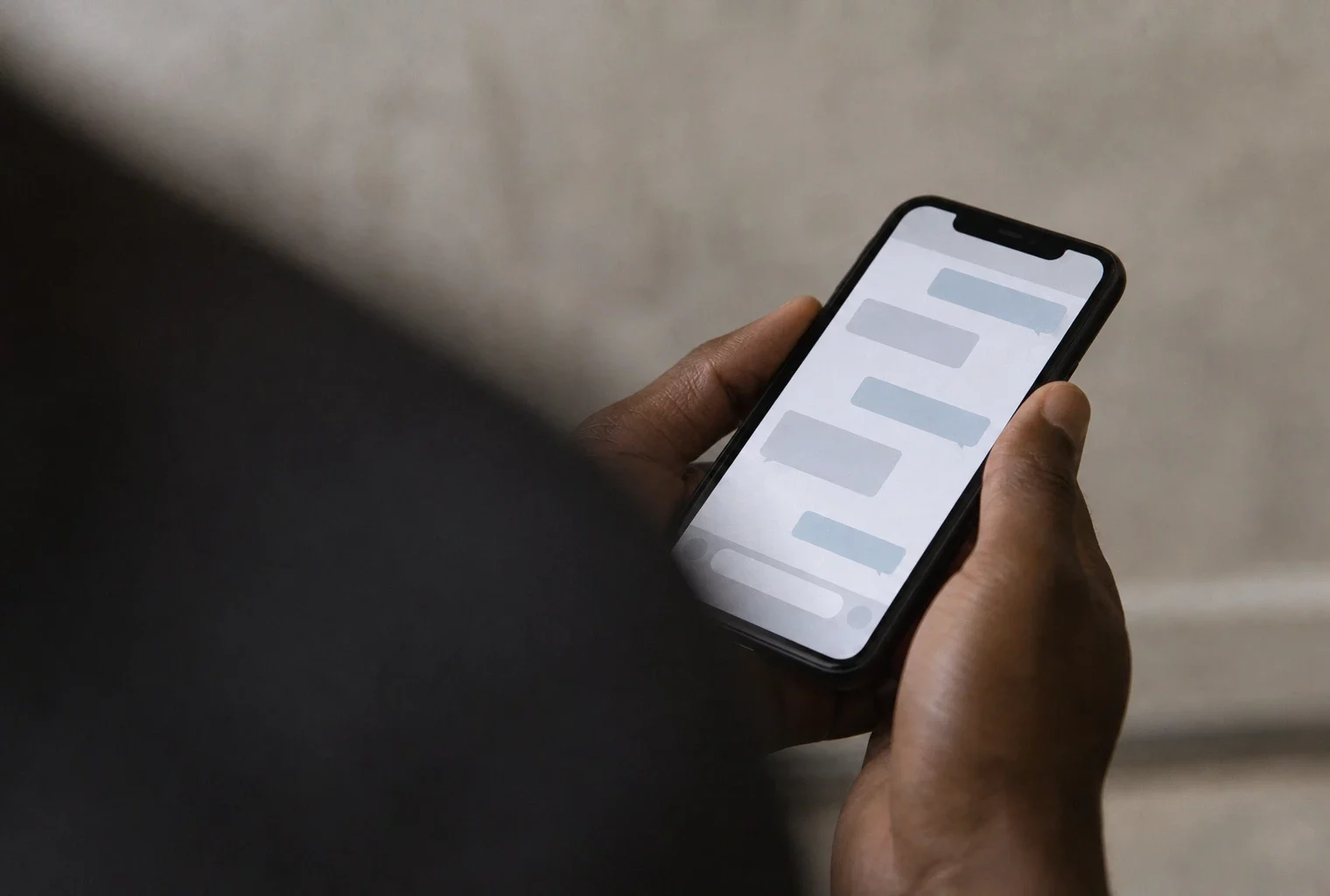 Gros plan en plongée oblique d’un téléphone tenu à la main, avec une conversation privée rendue illisible sur fond neutre.