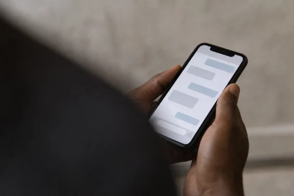 Gros plan en plongée oblique d’un téléphone tenu à la main, avec une conversation privée rendue illisible sur fond neutre.